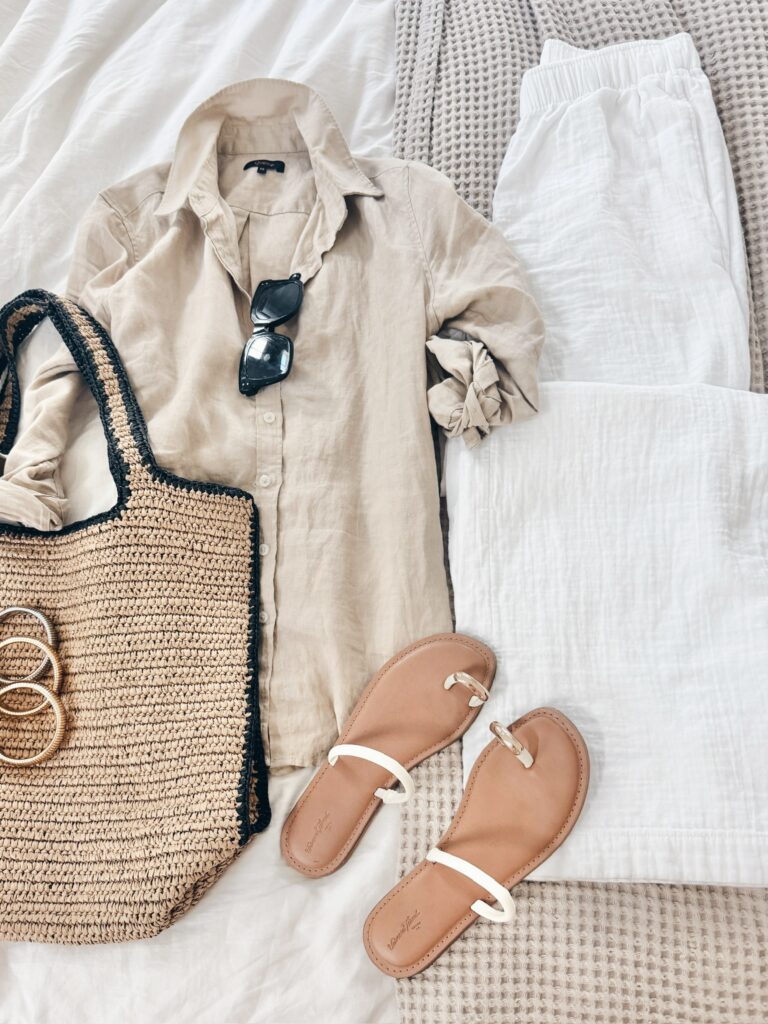 Neutral spring coastal outfit featuring a lightweight beige linen button-up, white gauzy pants, woven tote bag, minimalist sandals, and gold bangle bracelets.