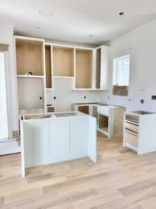 Guest kitchen under construction with light oak floors, farmhouse sink, and custom cabinetry.